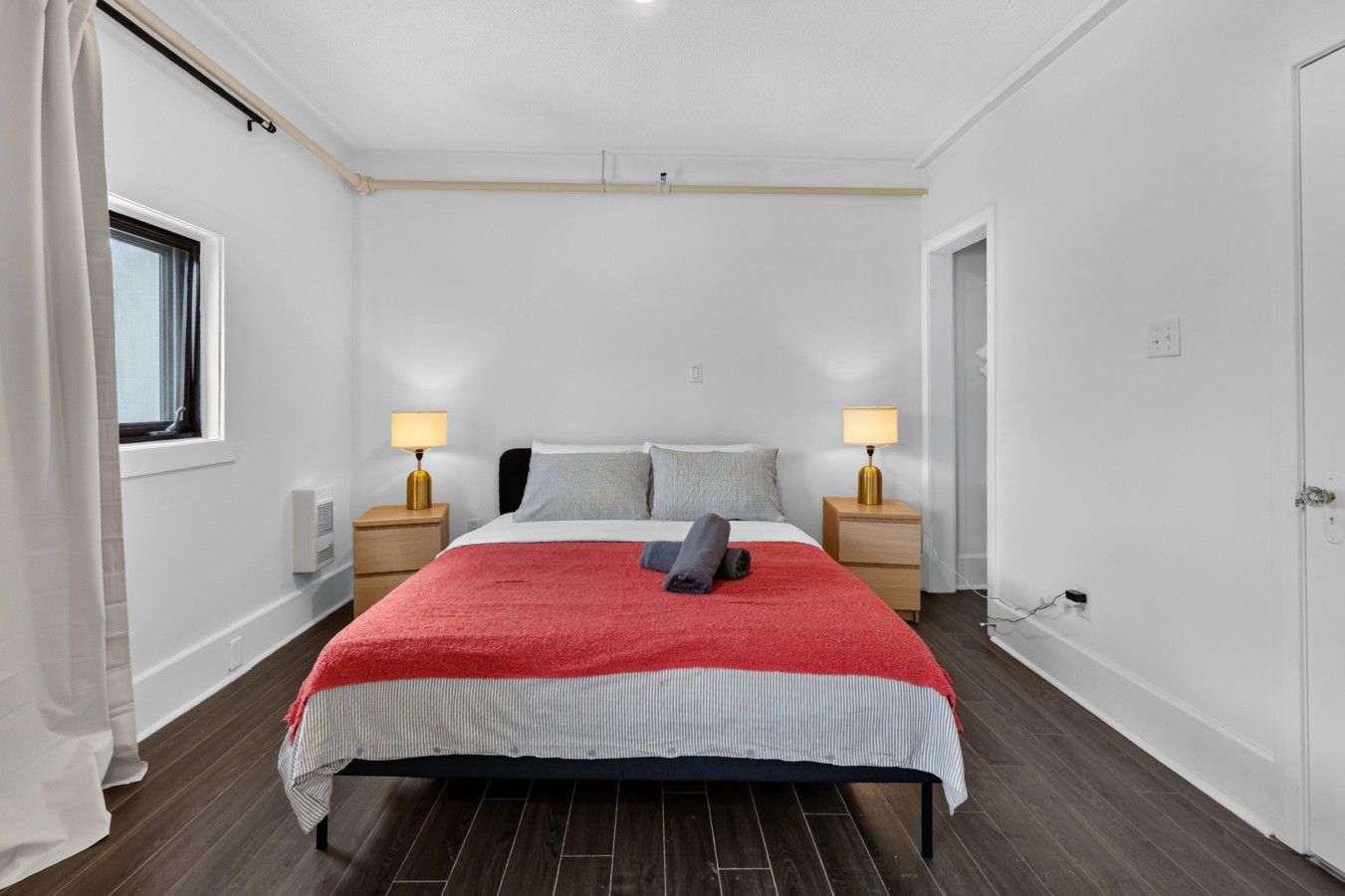 A hotel room with a bed, two bedside tables with lamps, a window, and a door.