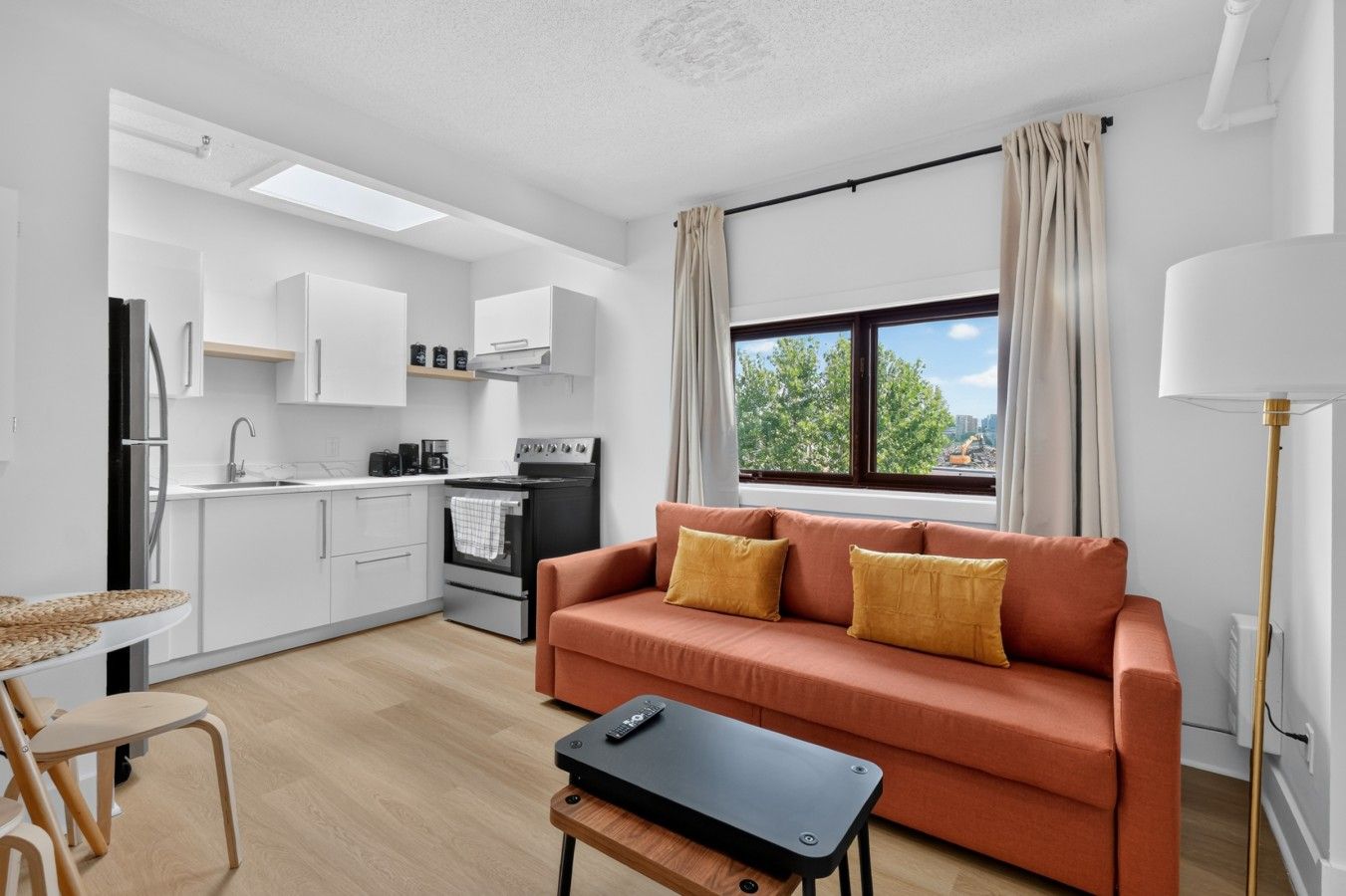 A compact living space with a kitchenette, a sofa, a dining area, and a window with a view.
