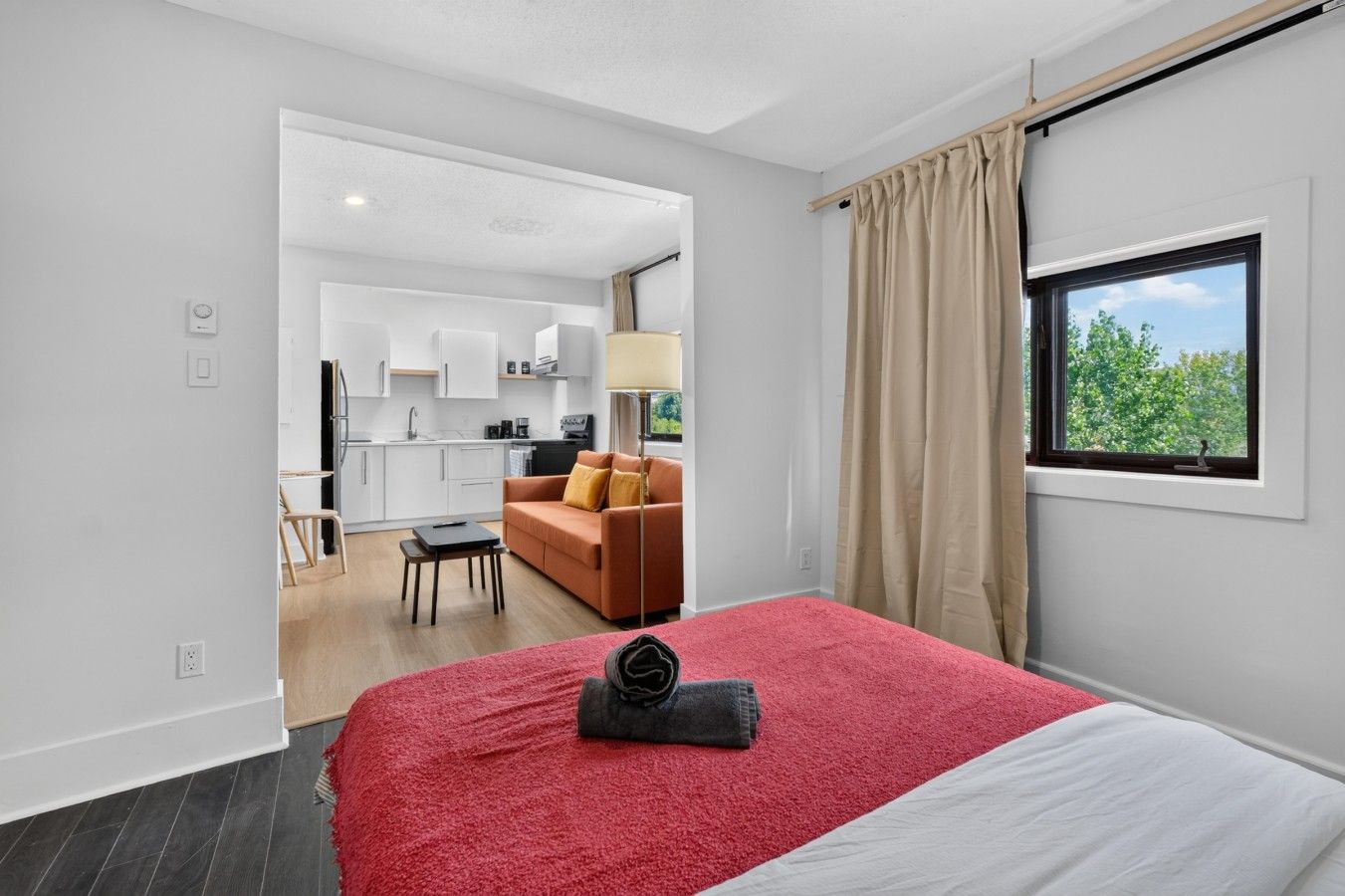 A modern hotel room with a large bed, a view of the outdoors, a kitchenette, and a seating area.
