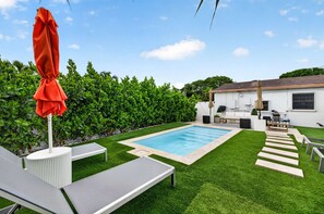 Ein Garten mit Schwimmbad, einer Terrasse mit Sitzgelegenheiten und einem gepflegten Heckenstreifen.