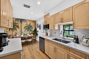 A modern kitchen with wooden cabinets, a built-in microwave, and a large window. - Casa Palma Heated Pool Hot Tub Games (Fort Lauderdale)