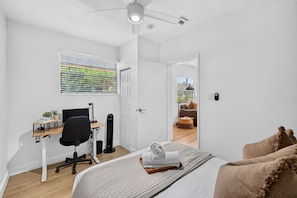A bedroom with a bed, a desk with a chair, a standing fan, and a window with blinds. - Casa Palma Heated Pool Hot Tub Games (Fort Lauderdale)