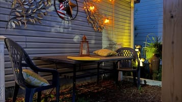 Un espacio de patio al aire libre con mesa y sillas, luces colgantes, decoración en la pared y un farol.