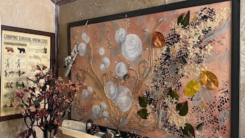 A wall with a framed artwork depicting a tree with leaves and flowers, a shelf with decorative items, and a framed poster on the wall.