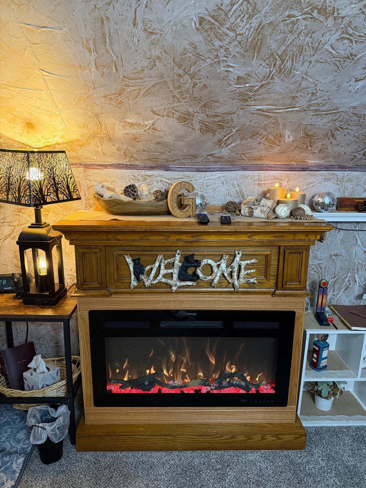 Een open haard met een 'WELCOME' bord, een lamp en decoratieve objecten op de schoorsteenmantel.