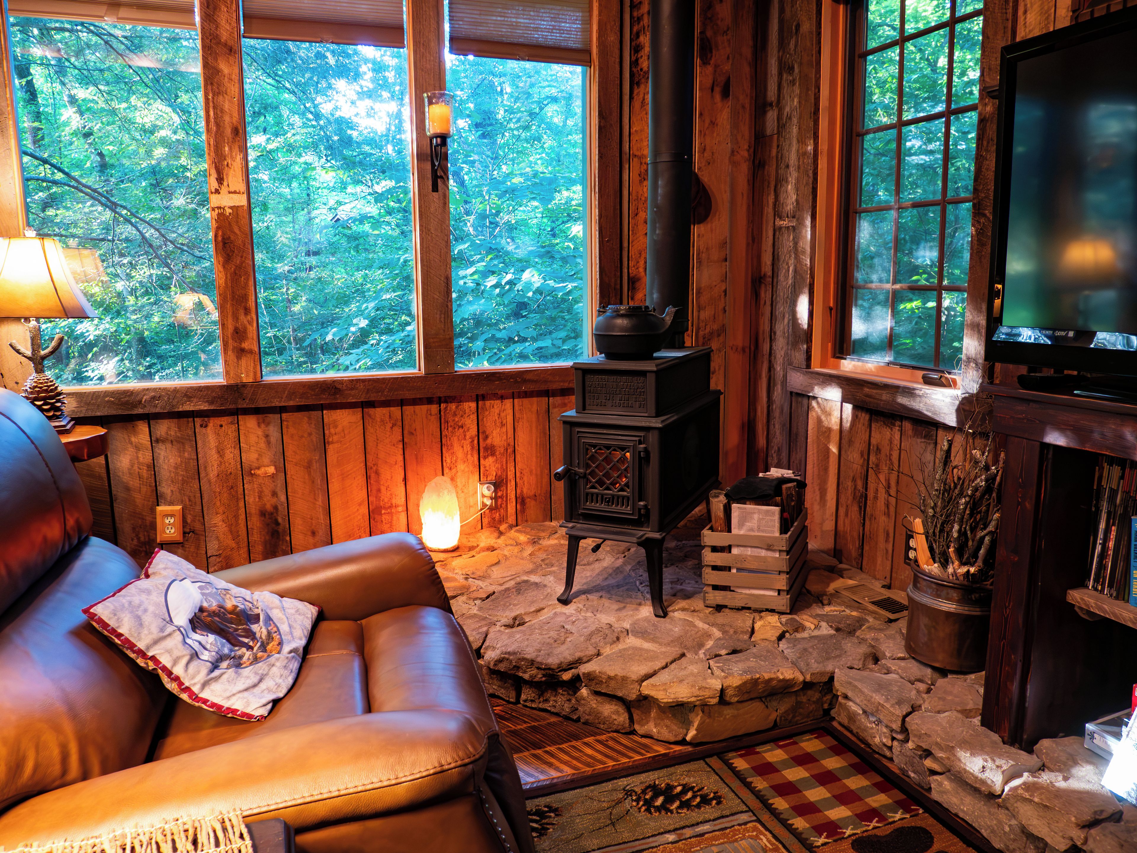 Un intérieur de chalet chaleureux avec une cheminée en pierre, un canapé en cuir et un téléviseur.