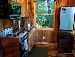 Eine Küche mit Holzausstattung, einem Edelstahlherd, einem Kühlschrank und einem Fenster mit Blick auf den Wald.
