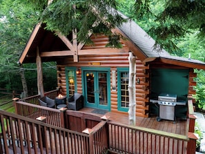 Eine Blockhütte mit einer Terrasse, Sitzgelegenheiten im Freien und einem Grill.