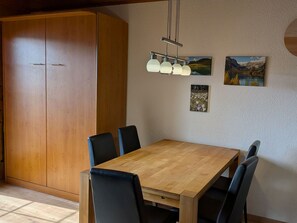 Ein Essbereich mit Holztisch und -stühlen, einem großen Kleiderschrank und Wandbildern.