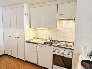 A compact kitchen with white cabinets, a stainless steel sink, a stove, and a microwave. - Residenz Albina Leukerbad # 4-bed apartment, Dusche, WC by Interhome (Leukerbad)