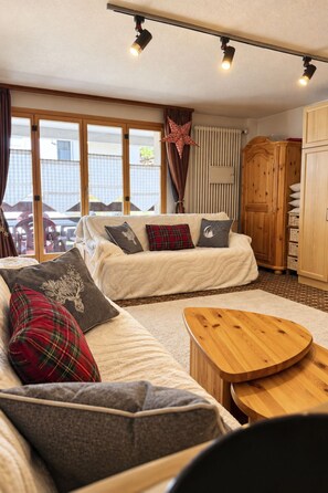 Ein gemütliches Wohnzimmer mit einer Sofagarnitur, einem Holztisch und einem großen Fenster mit Vorhängen.
