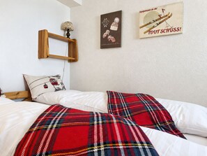 A bedroom with a bed, pillows, a blanket, a wooden shelf, and wall decorations. - Residenz Albina Leukerbad # 4-bed apartment, Dusche, WC by Interhome (Leukerbad)