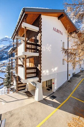Ein zweistöckiges Gebäude mit der Aufschrift 'ALBINA', einem Balkon im oberen Geschoss und einem verschneiten Berg im Hintergrund.