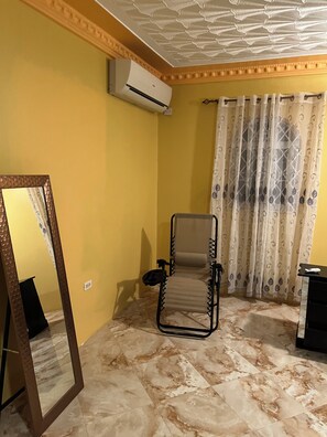 Une pièce comprenant un seul fauteuil inclinable, un radiateur portatif, un miroir et un rideau à motifs.