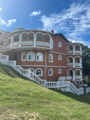 A multi-story building with balconies, a staircase, and a grassy slope. - Beautiful 4-bedroom apartment with AC in Saint Ann's Bay (Saint Ann's Bay)