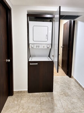A compact laundry room with a built-in washer and dryer, a small storage cabinet, and a door leading to another room. - Bello Apt en Playa El Angel, Pisicna +Vista al Mar (Pampatar)