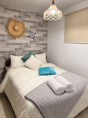 A bedroom with a bed, pillows, a blanket, a wall-mounted hat, a ship's wheel decoration, and a hanging light fixture. - Bello Apt en Playa El Angel, Pisicna +Vista al Mar (Pampatar)