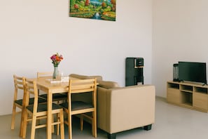 Una sala de estar moderna con una mesa de comedor, sillas, un sofá, una cafetera, un televisor y un cuadro en la pared.