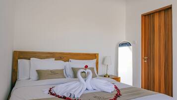 A hotel room with a neatly made bed, a wooden headboard, a nightstand with a lamp, and a wooden door.
