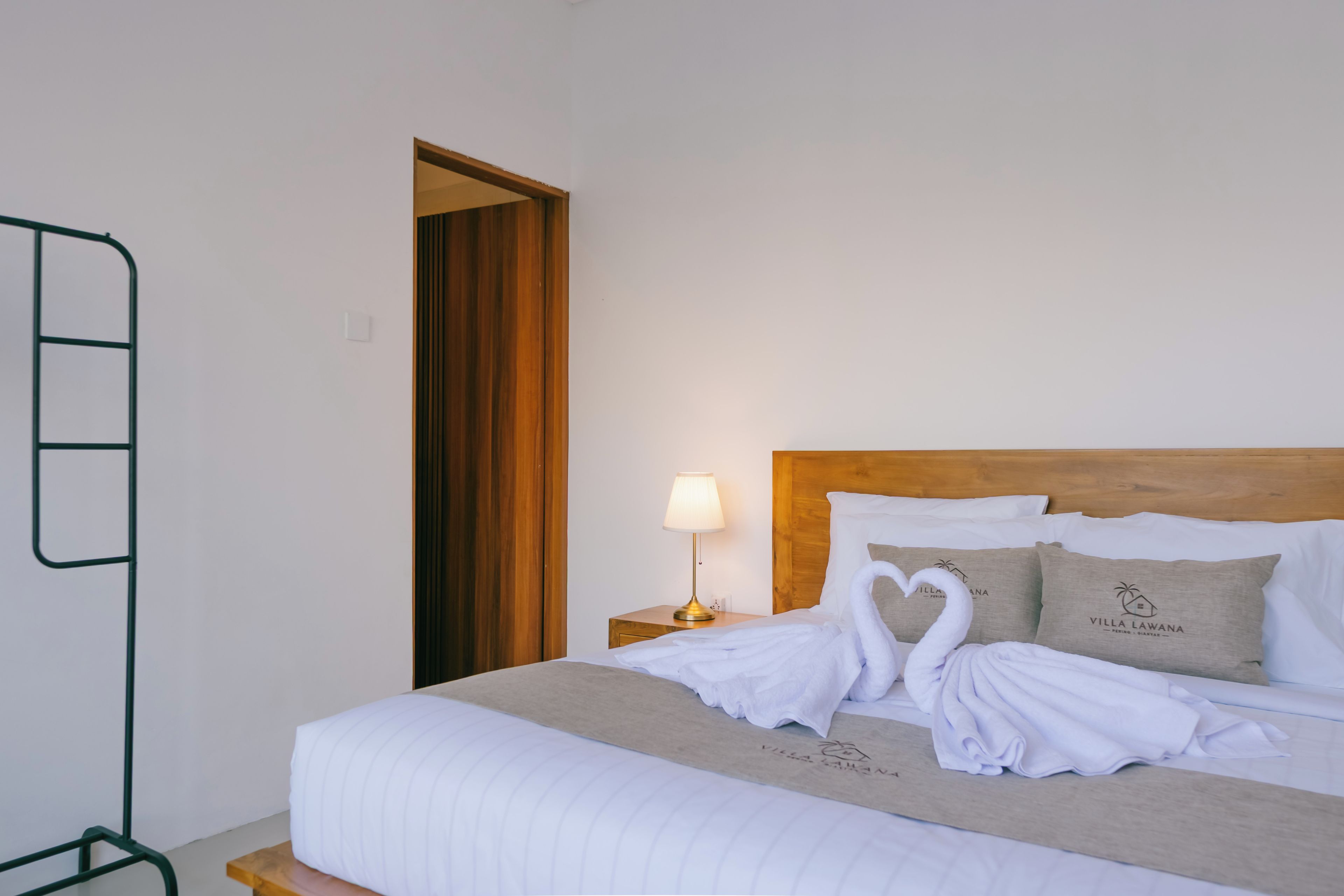 A neatly made bed with a heart-shaped towel arrangement, a bedside lamp, and pillows with a logo.