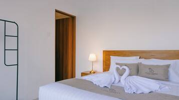 A neatly made bed with a heart-shaped towel arrangement, a bedside lamp, and pillows with a logo.