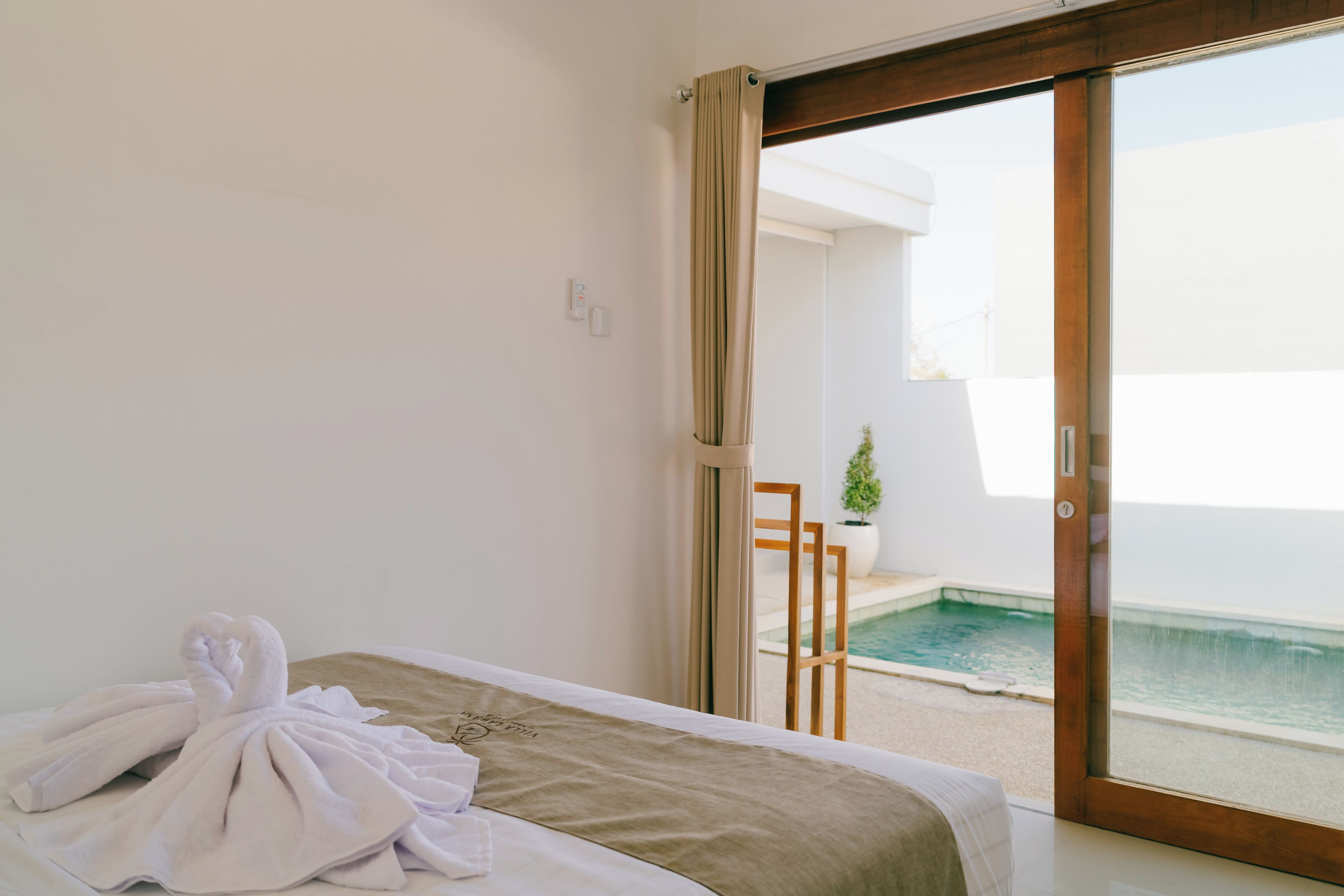 Een hotelkamer met een bed, een handdoek, een tafeltje en uitzicht op een zwembad.