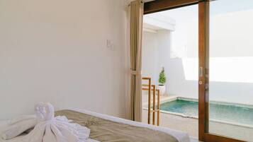 Una camera d'albergo con un letto, un asciugamano, un tavolino e vista sulla piscina.