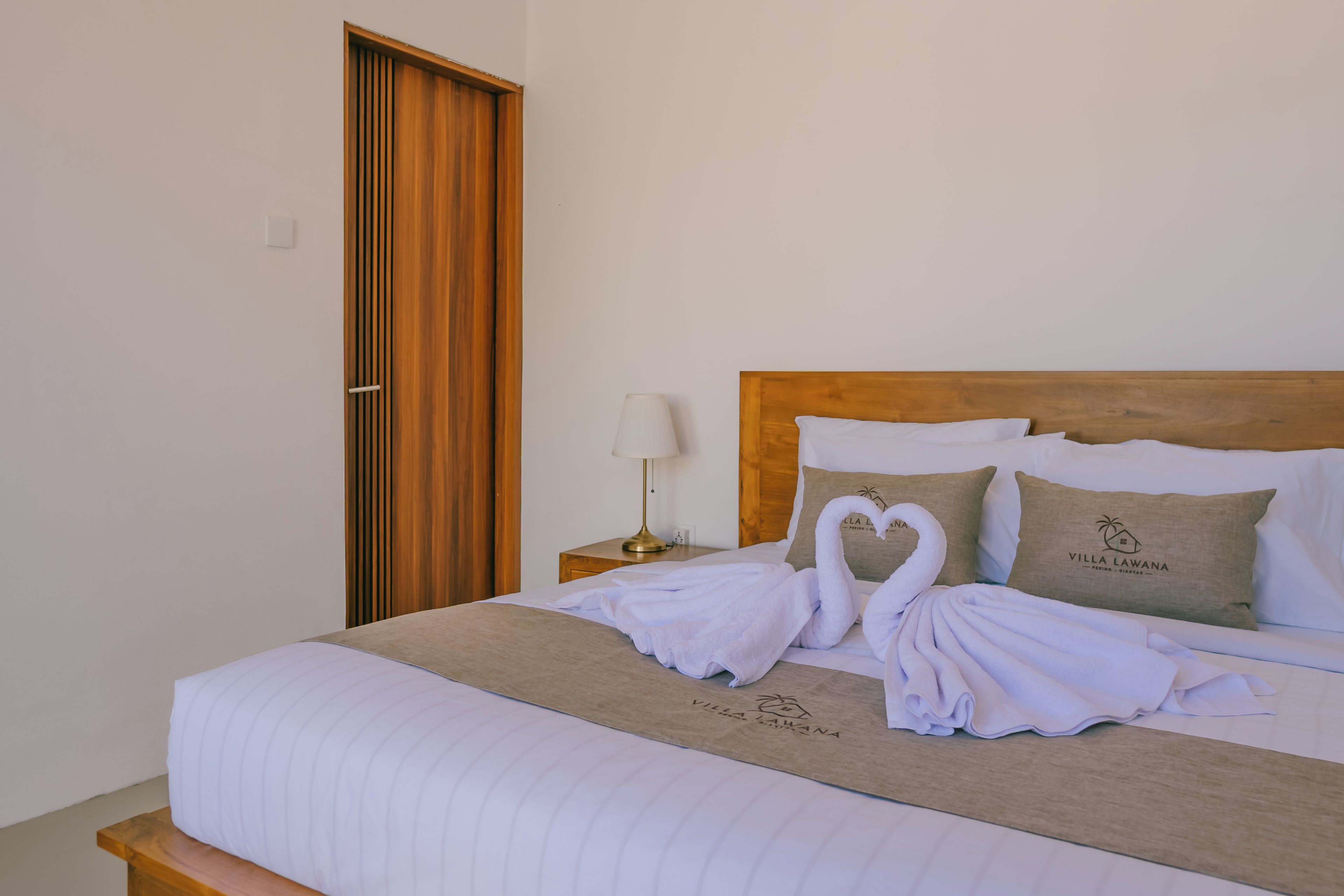 A hotel room with a bed, a wooden headboard, a nightstand with a lamp, and a door.