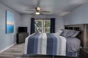 A bedroom with a bed, a ceiling fan, a TV on a dresser, and a window with curtains. - Kozy Cabin On the Lake (Stoughton)