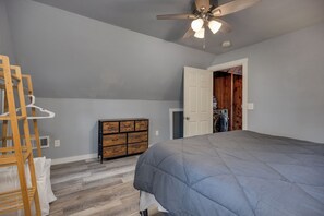A bedroom with a bed, a wooden dresser, a ceiling fan, and a door leading to a laundry area. - Kozy Cabin On the Lake (Stoughton)
