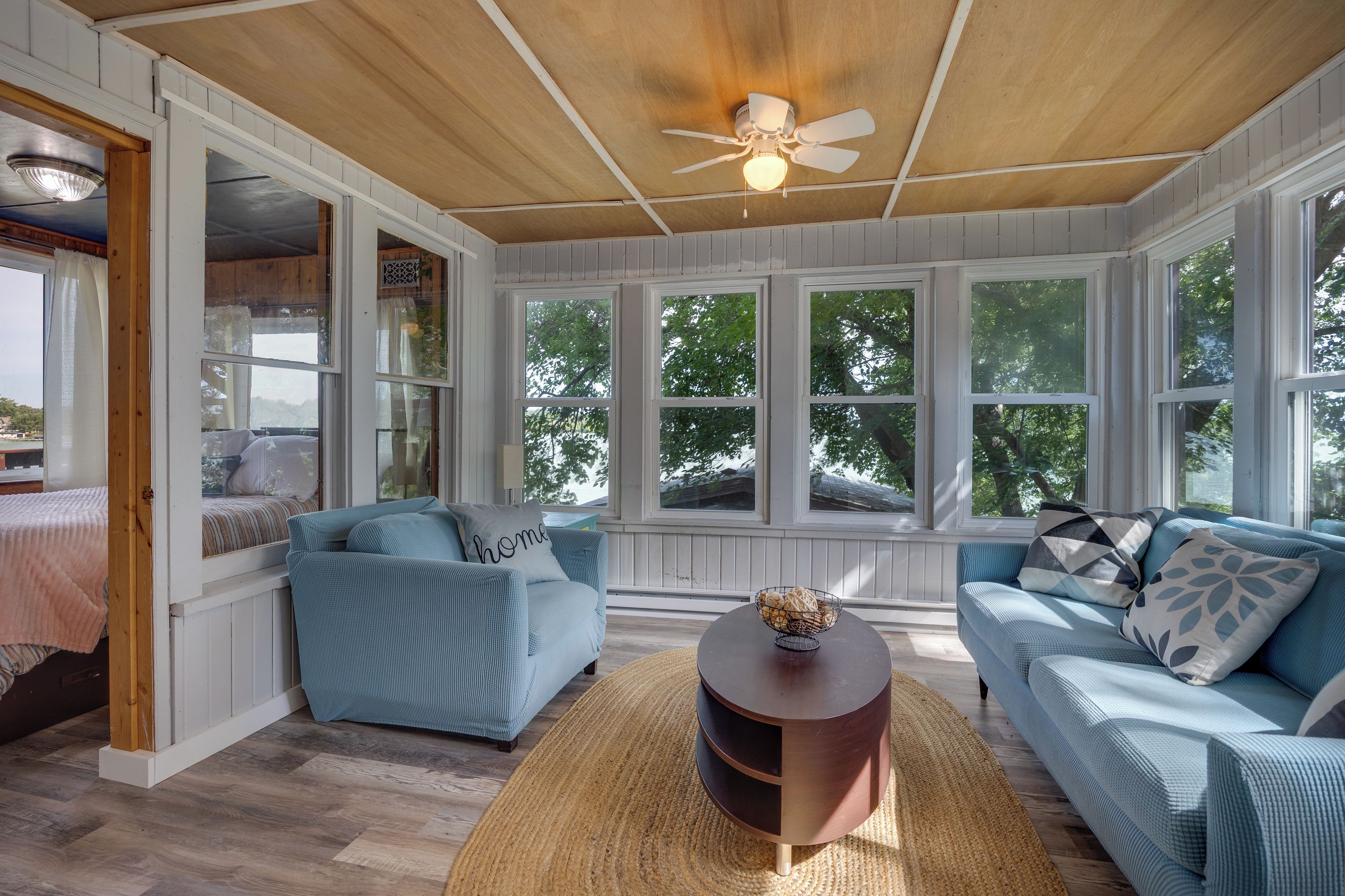A room with a wooden ceiling, a ceiling fan, and large windows.