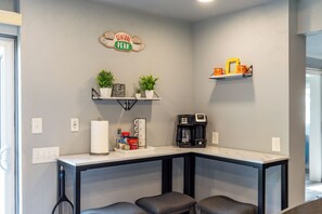 Ein Küchenbereich mit einer Kaffeemaschine, einem Schild mit der Aufschrift 'Central Perk' und zwei Zimmerpflanzen auf Regalen.