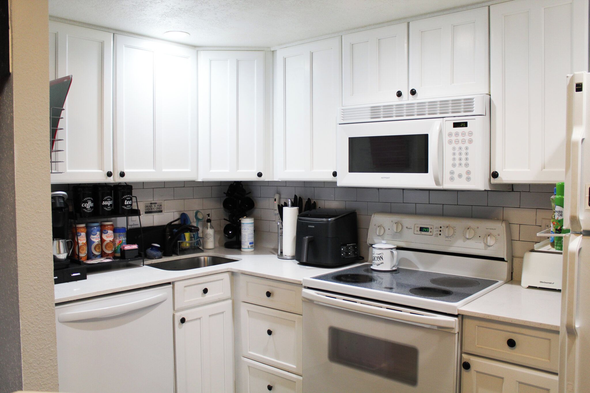 A kitchen with white cabinets, a microwave, a stove, a coffee maker, and various kitchen utensils.