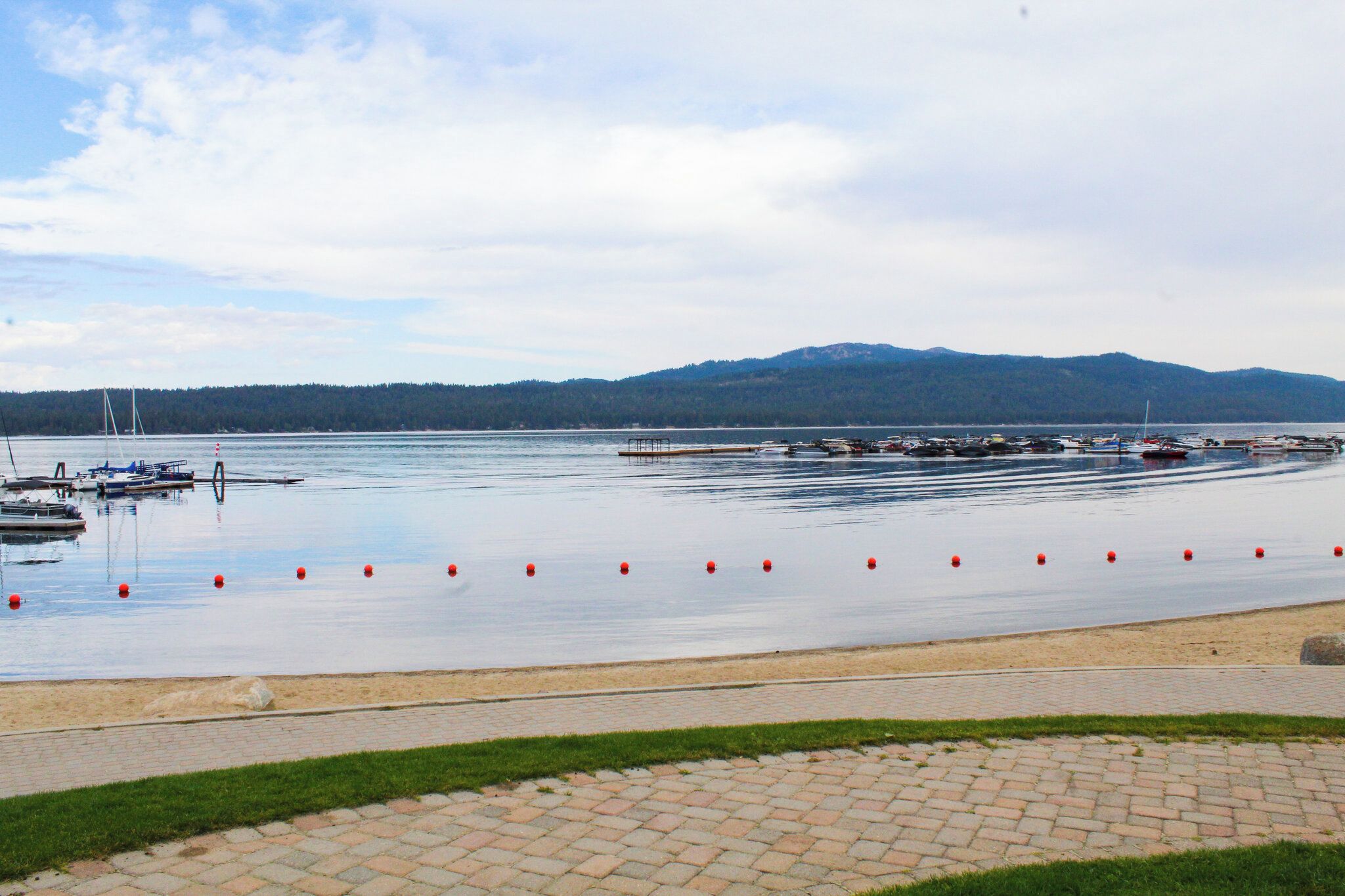 Un lac paisible, avec des bateaux amarrés sur la rive et une colline boisée en arrière-plan.