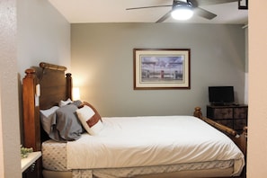 Un dormitorio con cama, mesita de noche, televisor y ventilador de techo.