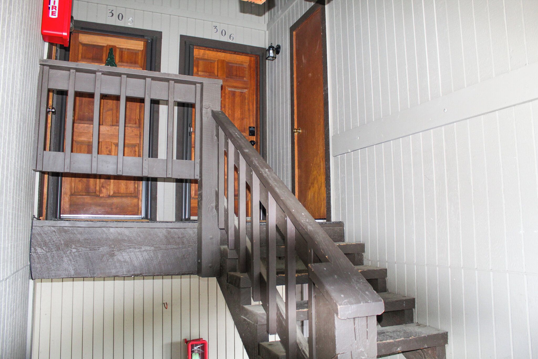 Un escalier en bois avec une rampe métallique menant à une porte dotée d’une fenêtre.