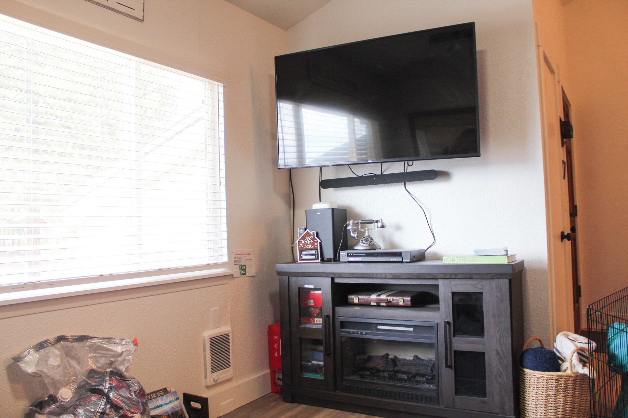 A room with a flat-screen TV mounted on the wall, a window with blinds, a fireplace, and a bookshelf.