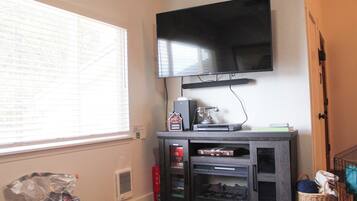 A room with a flat-screen TV mounted on the wall, a window with blinds, a fireplace, and a bookshelf.