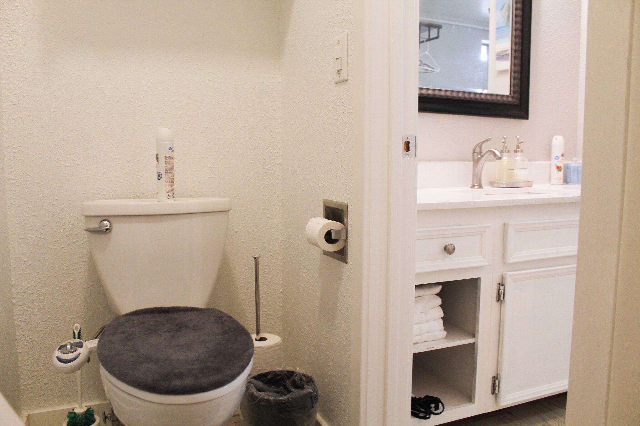 Een badkamer met toilet, toiletpapier, een prullenbak en een wastafel met spiegel erboven.