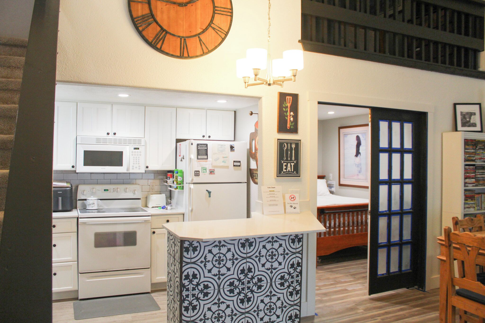 A kitchen with white cabinets, a microwave, a refrigerator, and a clock on the wall.