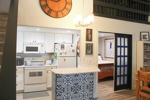 Una cocina con armarios blancos, un microondas, un refrigerador y un reloj en la pared.