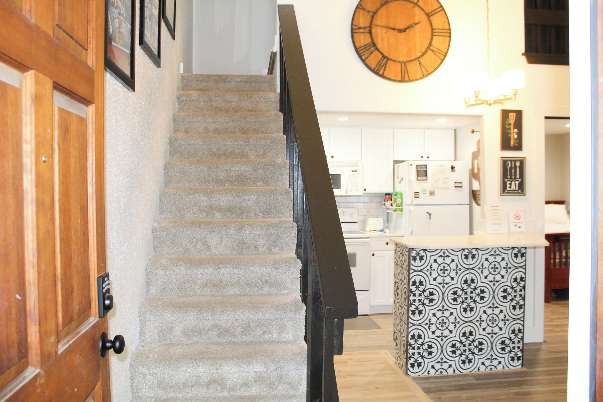 Un escalier menant à une cuisine, avec une horloge au-dessus.