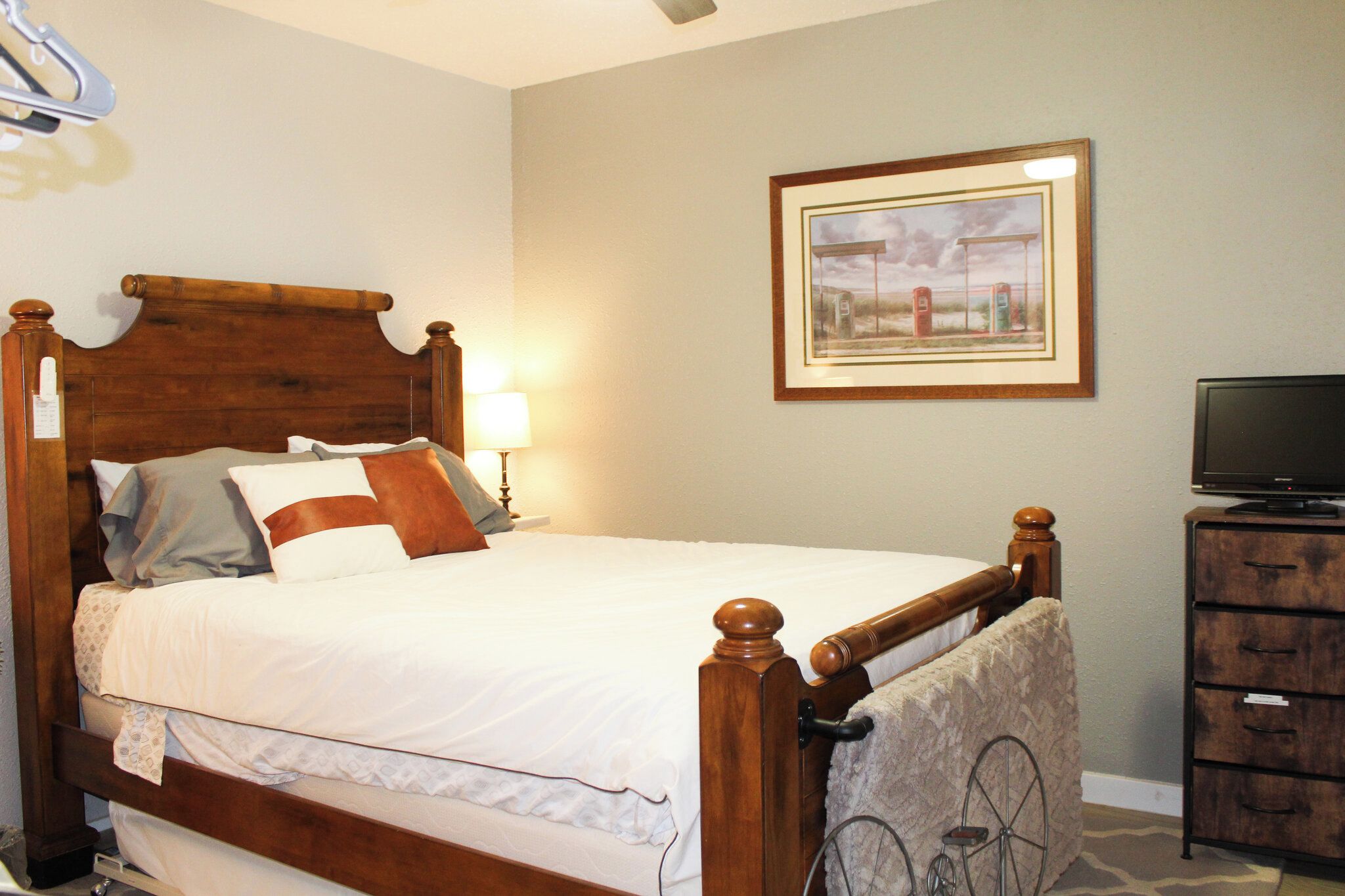 A neatly made bed with a wooden headboard, a lamp, a framed picture on the wall, and a television on a wooden stand.