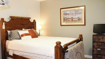 A neatly made bed with a wooden headboard, a lamp, a framed picture on the wall, and a television on a wooden stand.