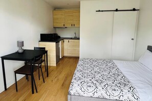 Ett litet rum med en säng, ett litet matbord, en stol, en mikrovågsugn och ett litet pentry.