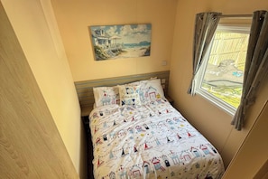 Ein Schlafzimmer mit einem Bett, einem Bild einer Strandansicht und einem Fenster mit Vorhängen.