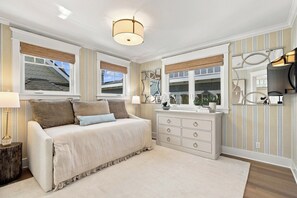 Ein Schlafzimmer mit Bett, Kommode, Spiegel und einem Fenster mit Jalousien.