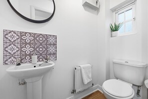 Une salle de bain avec un lavabo blanc, des toilettes et une fenêtre agrémentée d’une plante.