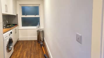 A compact kitchen with a washing machine, a window, and a trash bin.