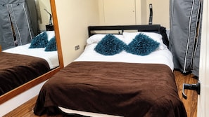 A hotel room with a bed, a mirror, a wardrobe, and a door.